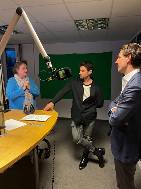 Interviewpartner im Studio Drei Personen in einem Studio, eine spricht ins Mikrofon, zwei andere lauschen.