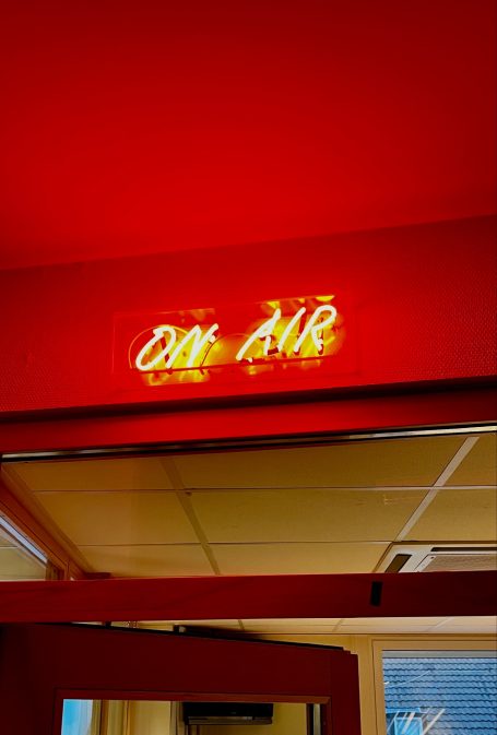 Das Eli "On Air" Neonzeichen "ON AIR" an einer roten Wand.