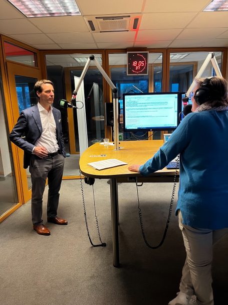 Interview in angenehmer Studio-Atmosphäre Mann im Anzug spricht mit Frau am Tisch in einem Radiostudio.